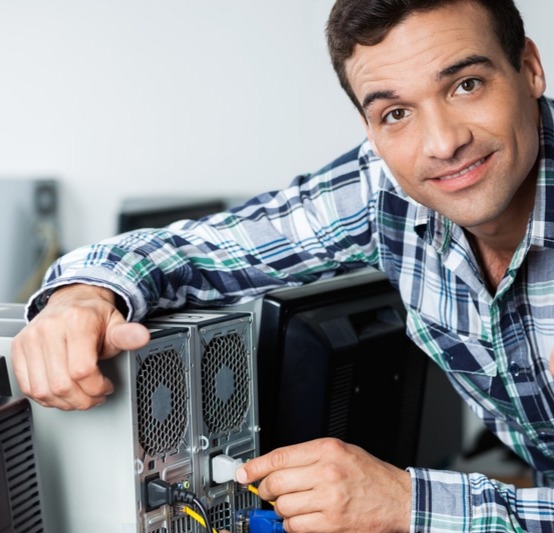 Man in plaid shirt plugging an Ethernet cable into the back of a desktop computer.