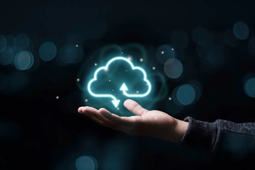 Hand holding a glowing cloud icon with upload and download arrows on a dark blurred background.