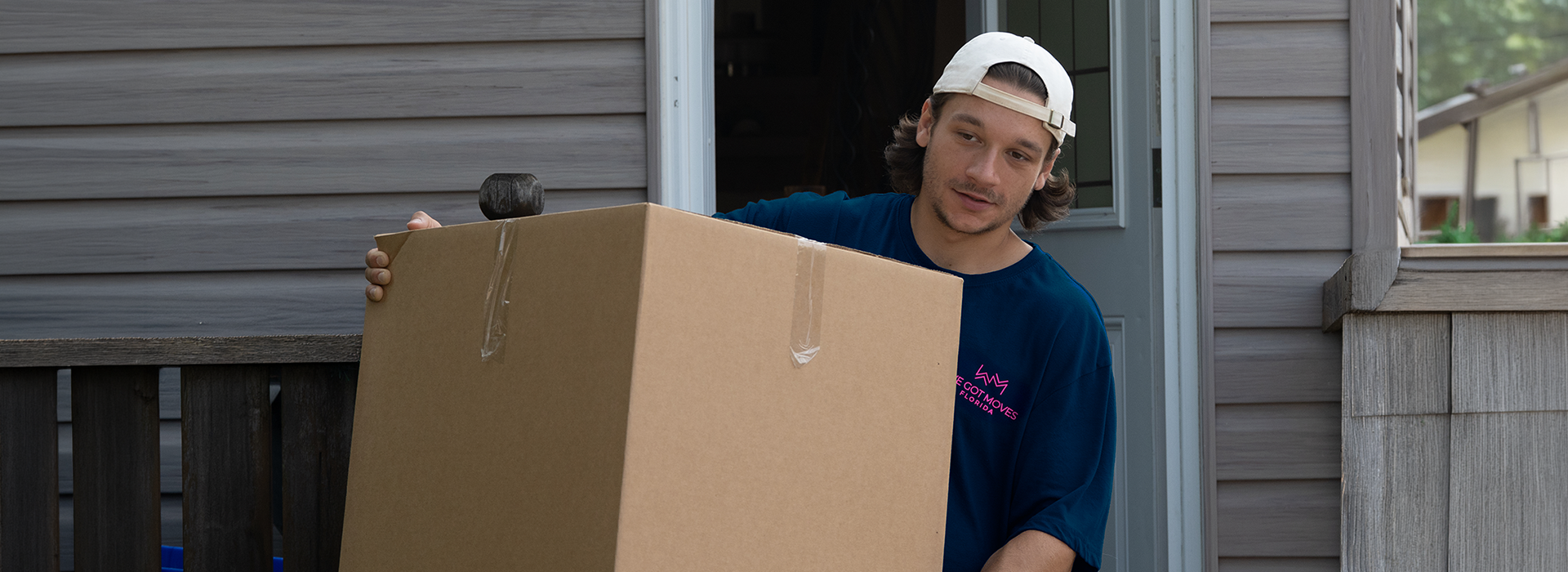 We Got Moves crew member in a navy company shirt carrying a large cardboard box out of a home