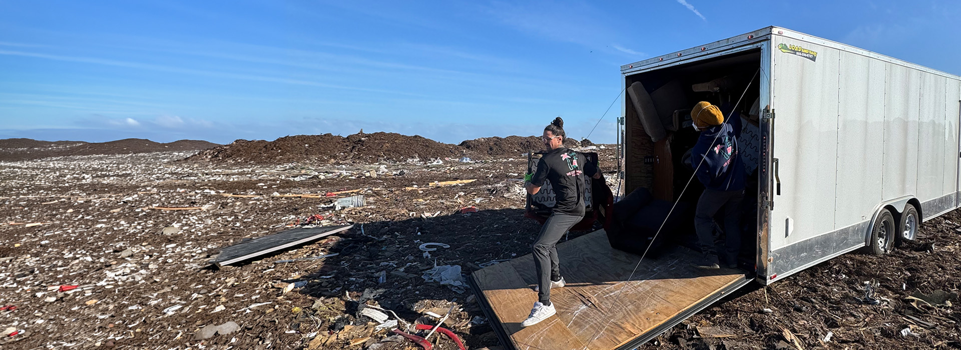 Two crew members unloading furniture from a white trailer at a Florida debris drop-off site