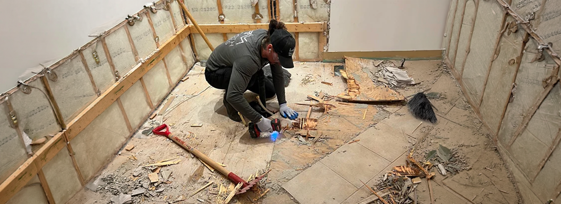 Worker removing old flooring in a gutted room during a small demolition project
