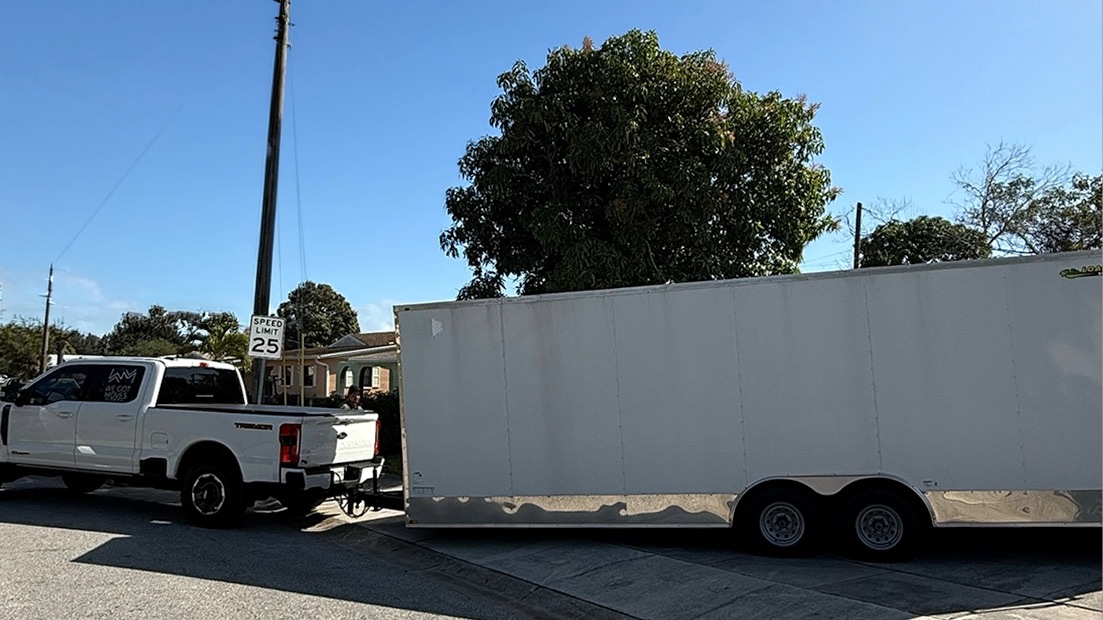 White We Got Moves pickup truck towing a large enclosed trailer on a residential street