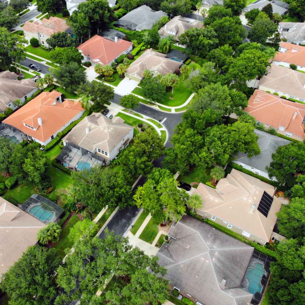 Aerial view of homes with terracotta roofs and screened pools on a tree-lined street in Lake Mary, Florida