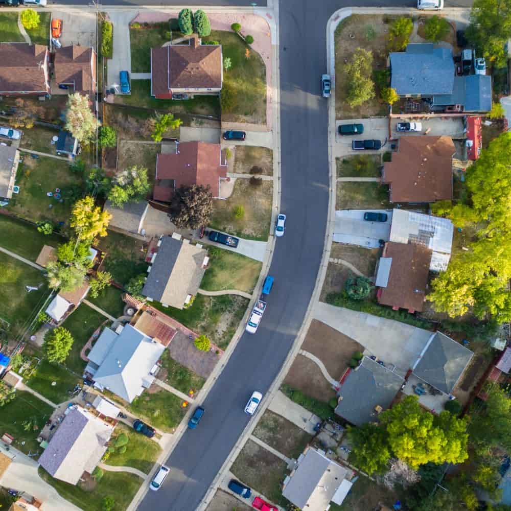 Overhead view of a residential street with houses, lawns and parked cars