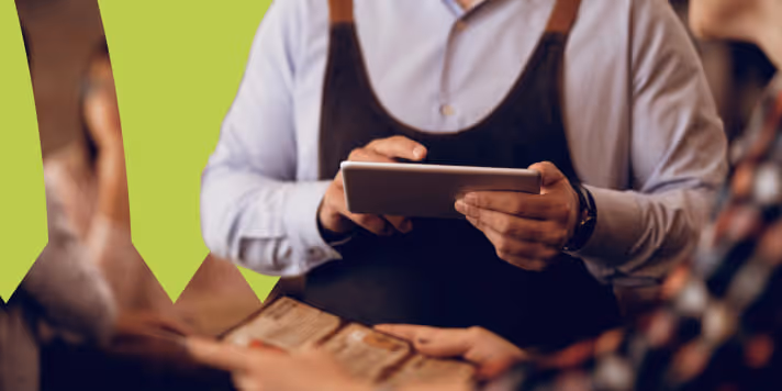 Garçom com avental usando um tablet para fazer pedidos para clientes em um restaurante.