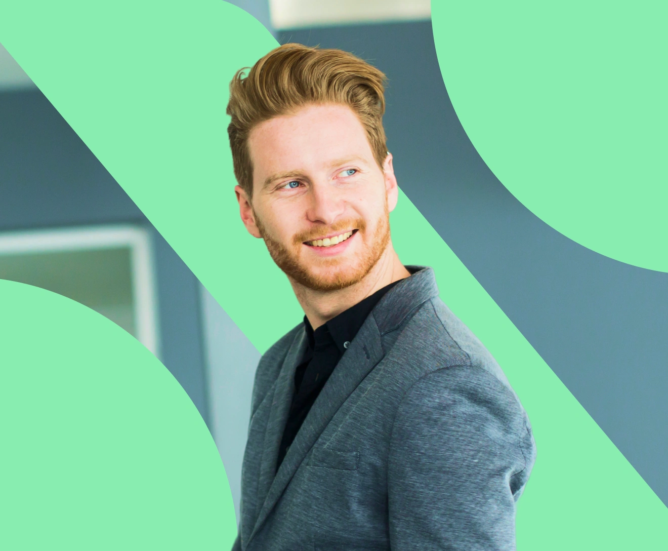 Smiling man with red hair and beard wearing a gray blazer looking to the side.