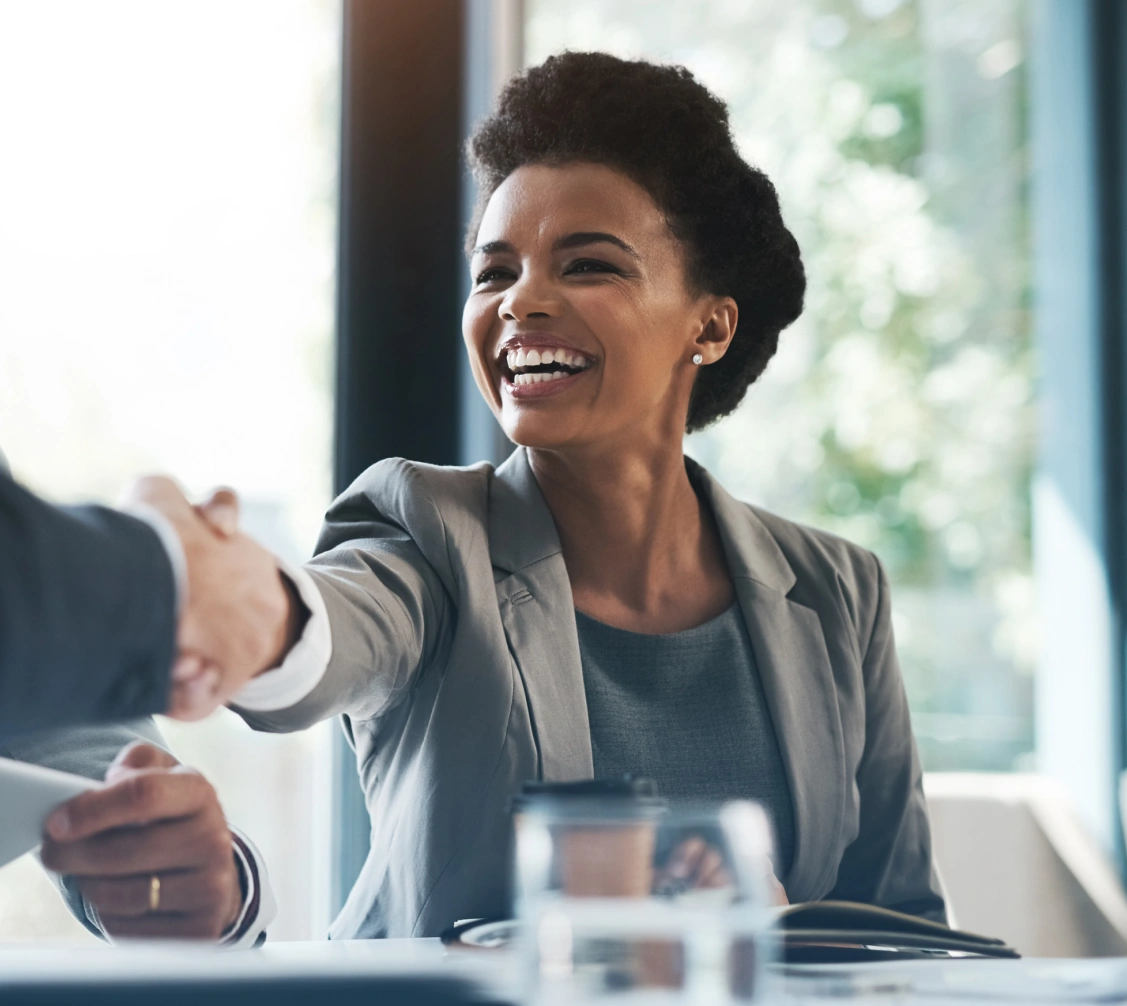 Smiling businesswoman shaking hands with a colleague in a bright office setting.