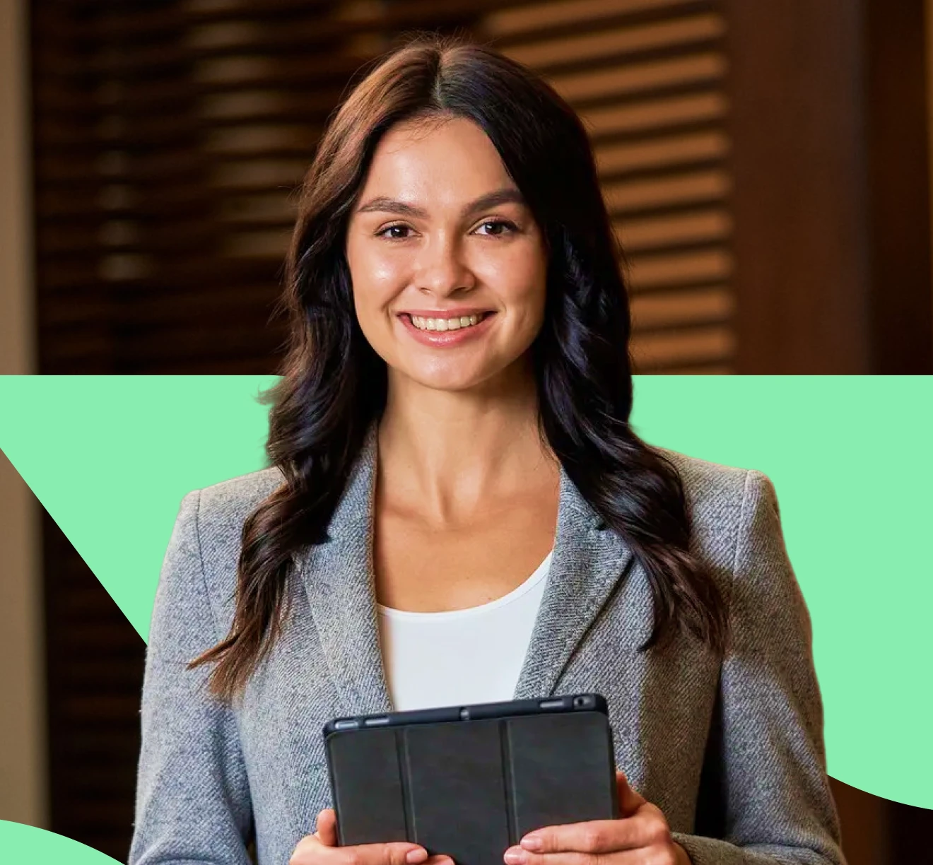 Smiling woman with long dark hair wearing a gray blazer holding a tablet.
