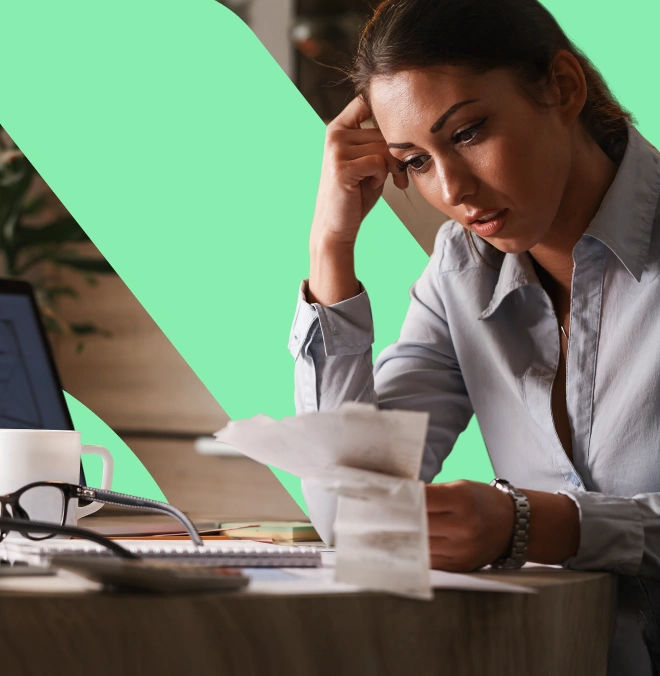 Woman sitting at a table looking stressed while reviewing receipts and bills.