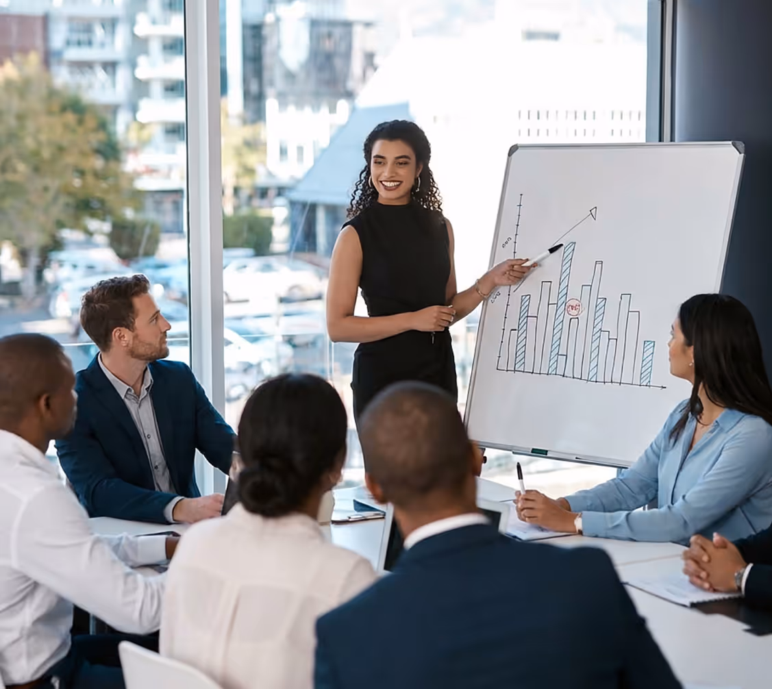 Businesswoman presenting a bar chart with an upward trend to a group of colleagues in a modern office.