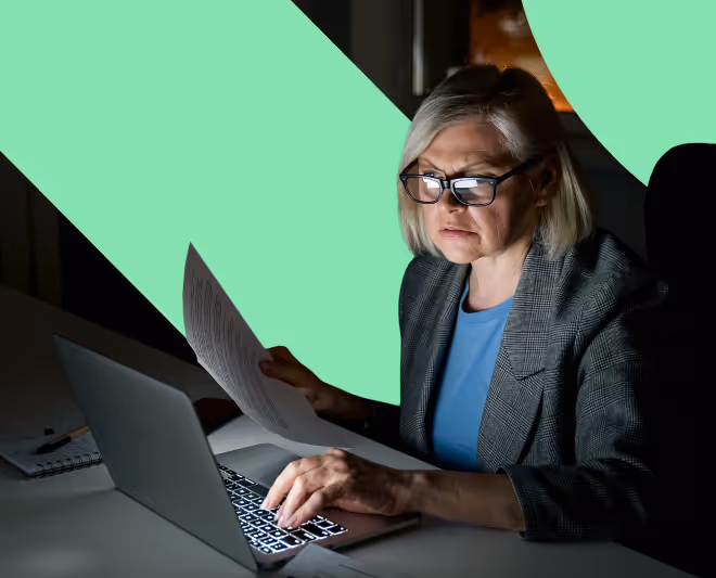 Older woman wearing glasses working on a laptop and holding a document in a dimly lit room, with the Smashing Numbers logo as a background visual effect.