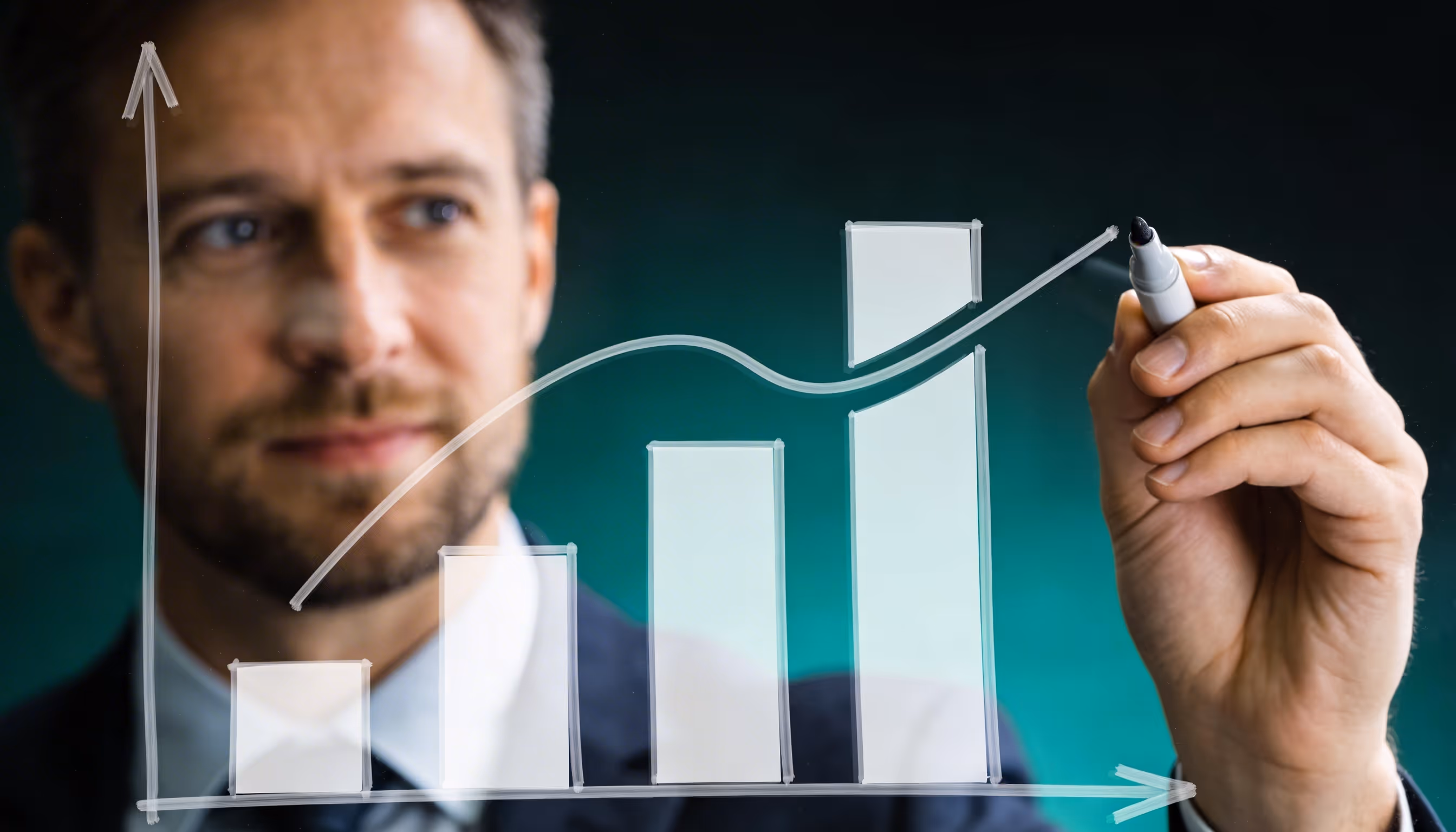 Man in suit drawing an upward-trending bar chart with three bars on transparent glass.