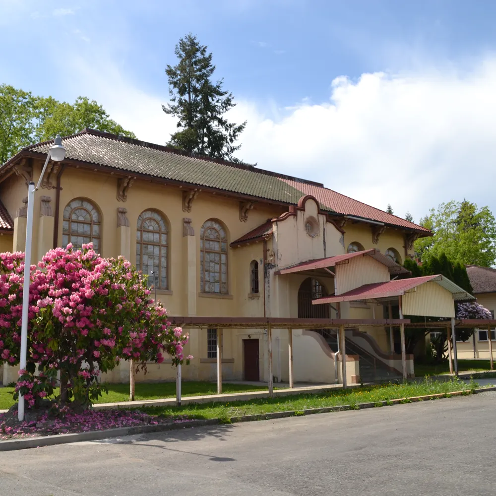 SWIFT Center The Hub Assembly Hall a historic spanish colonial revival building beside a paved road with flowers, trees, under blue skies with a few clouds
