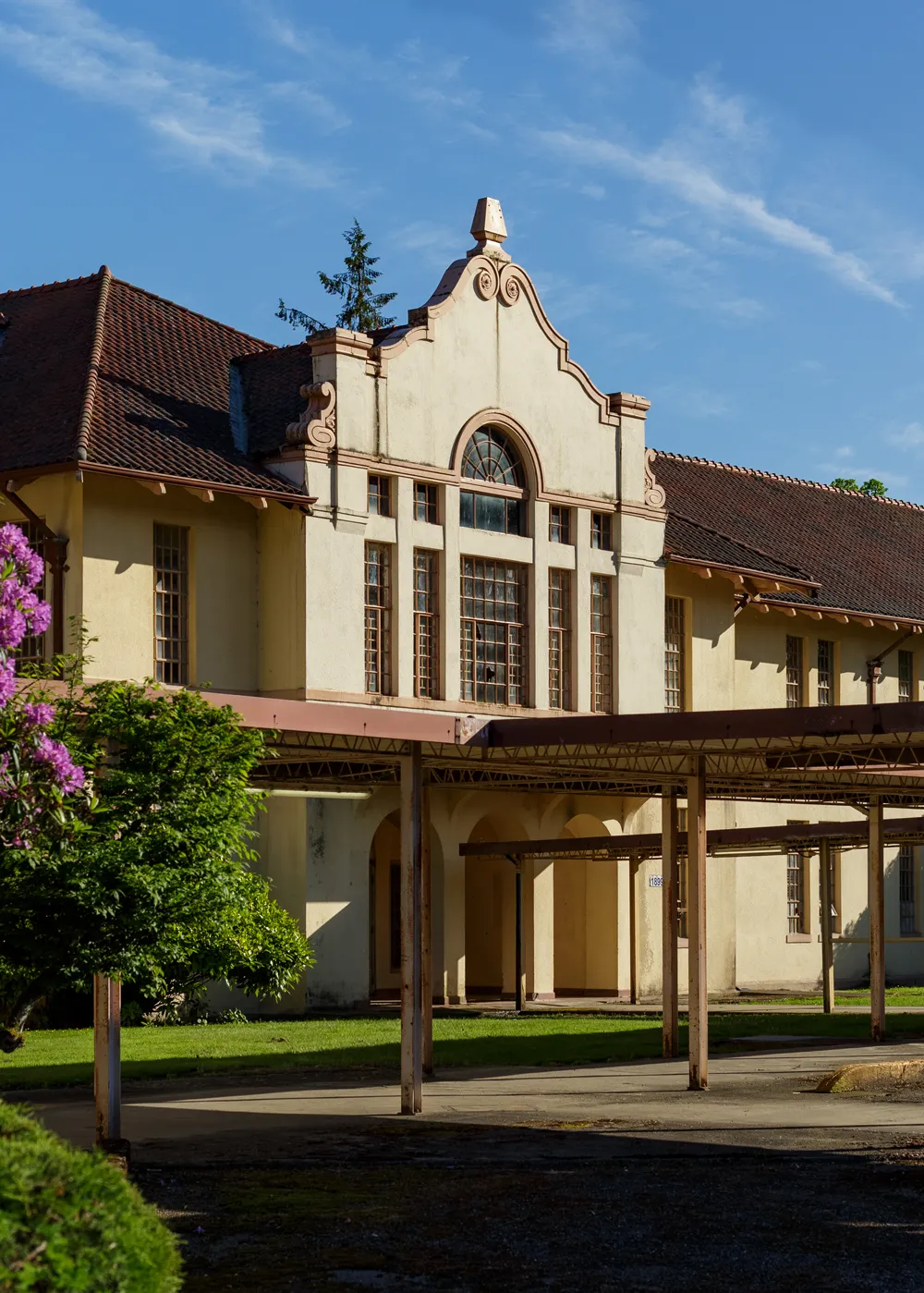 Adaptive reuse opportunity swift center sedro woolley spanish colorial revival building, tan with a red roof surrounded by greenery and with blue skies overhead.