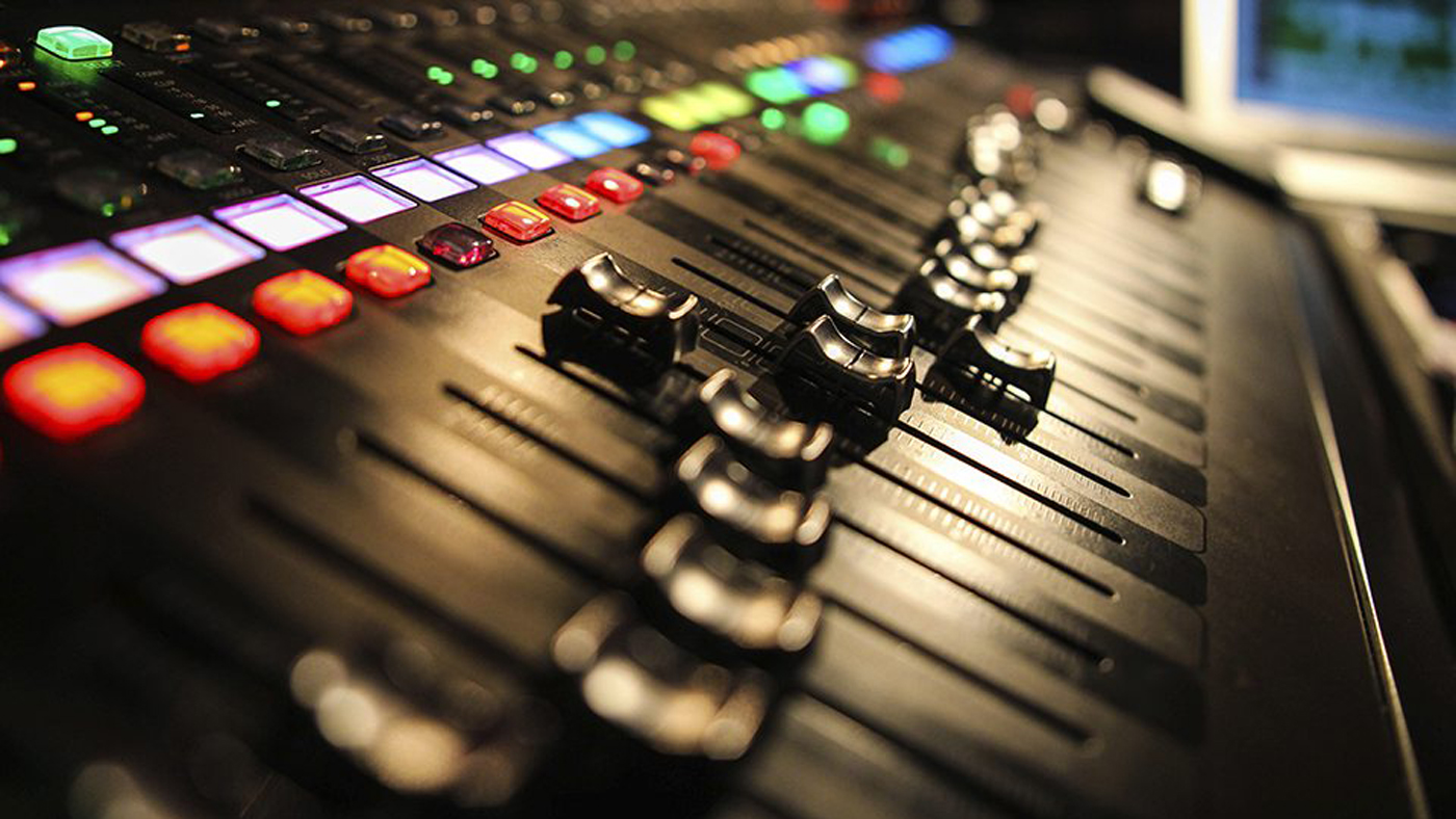 Close-up of audio mixer faders and illuminated control buttons in a recording studio.