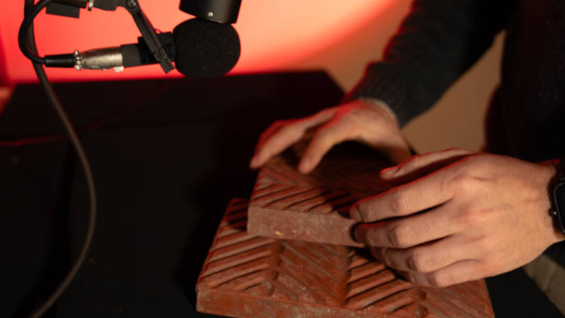 Hands holding a chocolate bar with geometric patterns near a microphone against a red background.