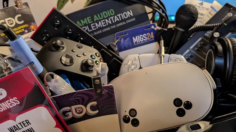 Open case filled with audio cables, headphones, gaming controller, game audio programming book, audio mixer, and event badges.