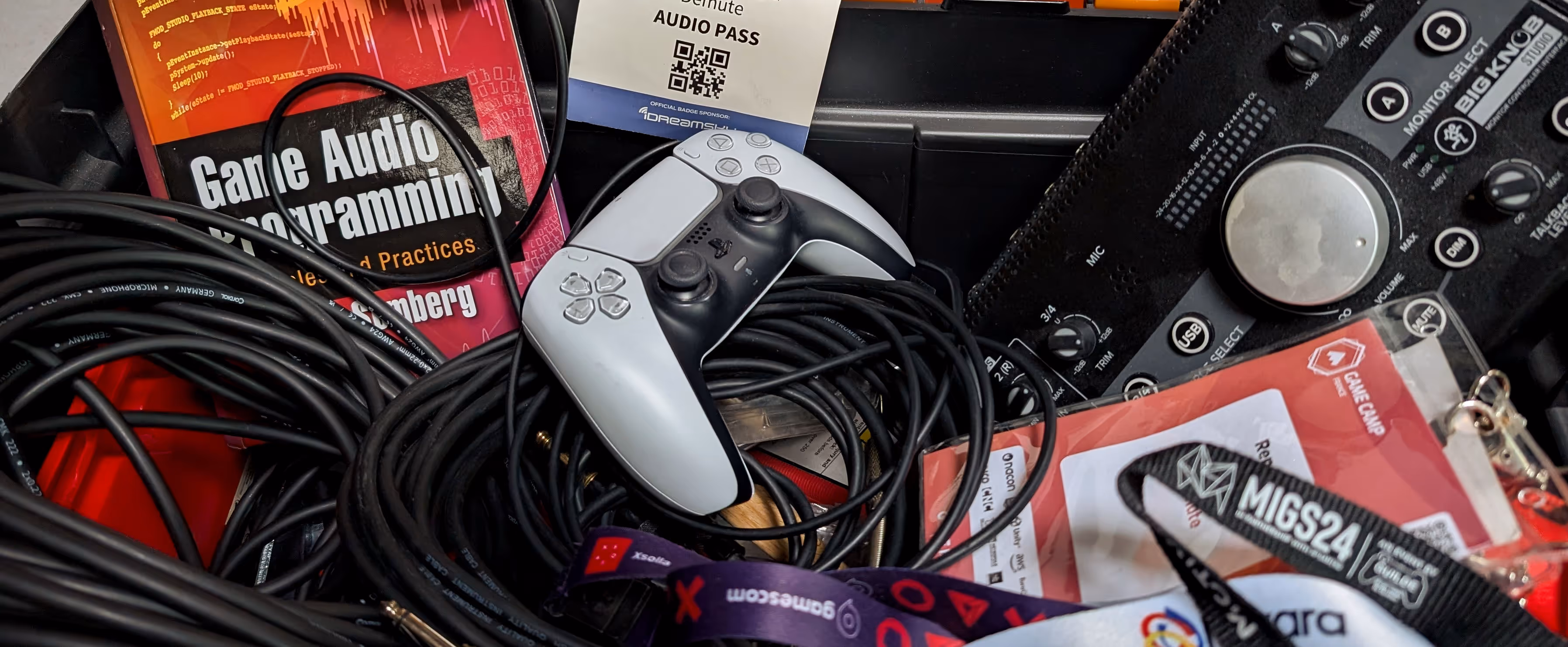 Game controller, audio cables, a Game Audio Programming book, and event passes with lanyards placed closely together.