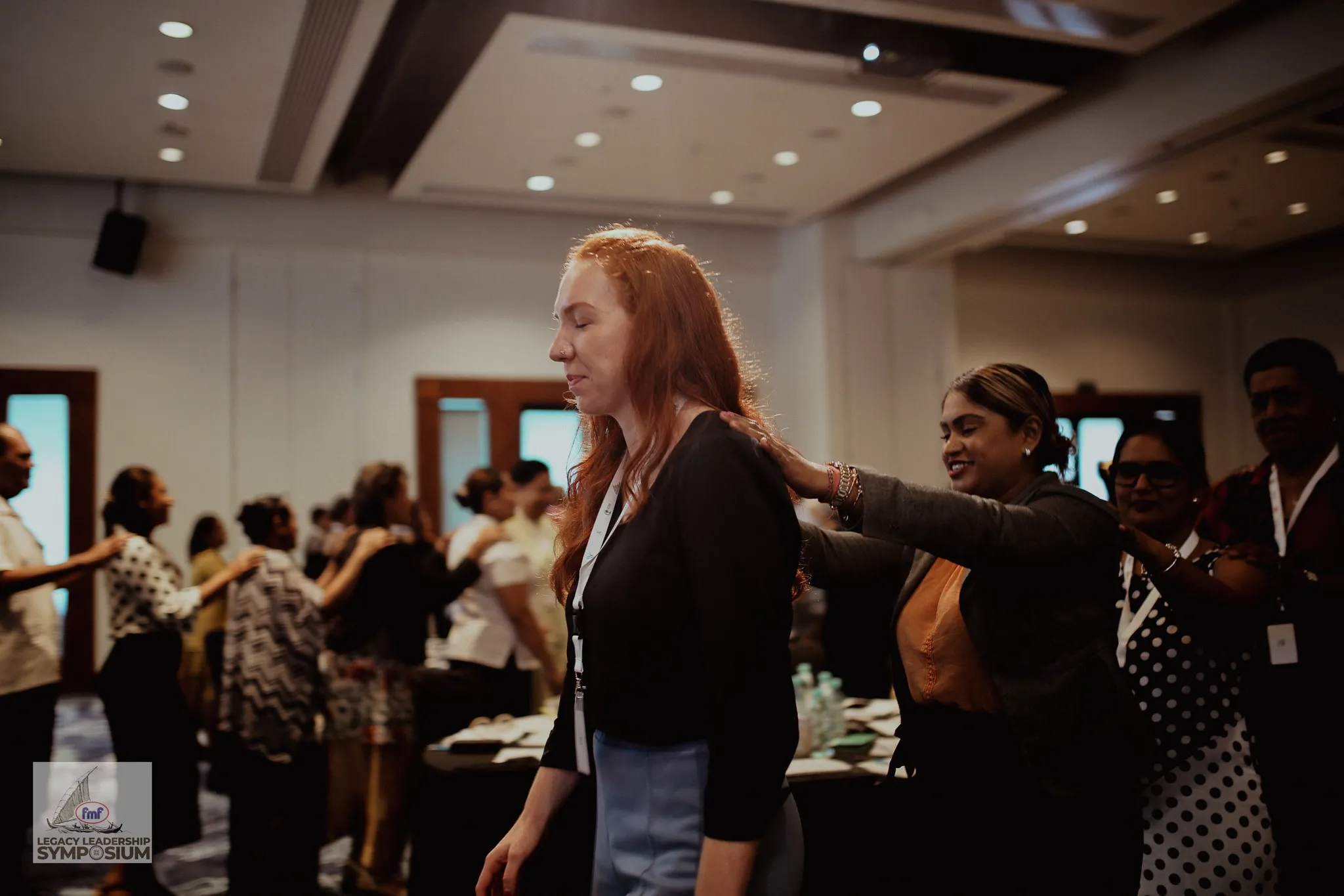 A group of people standing in a line giving each other shoulder massages during an indoor event.