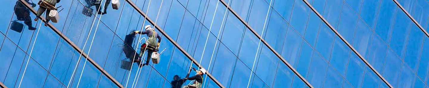 Workers suspended on ropes cleaning the windows of a tall glass building.