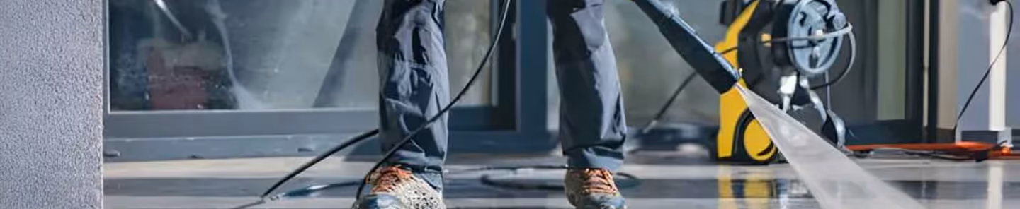 Person using a pressure washer to clean an outdoor floor near a building entrance.