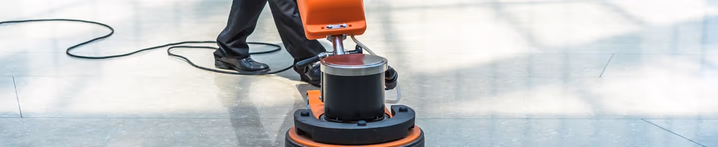 Person operating an orange floor polishing machine on a shiny tiled floor.