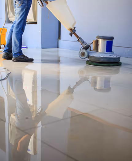 Person using a floor scrubber machine to clean a shiny tiled floor indoors.