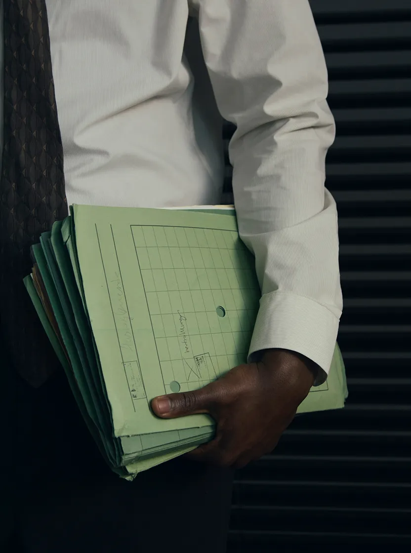 Une personne vêtue d'une chemise blanche et d'une cravate sombre tenant un gros dossier vert sous le bras.