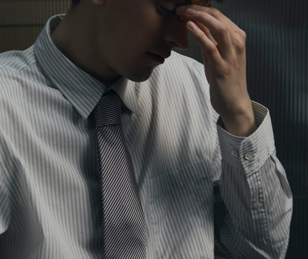 Homme en chemise rayée et cravate tenant sa tête avec une main, semblant stressé ou préoccupé.