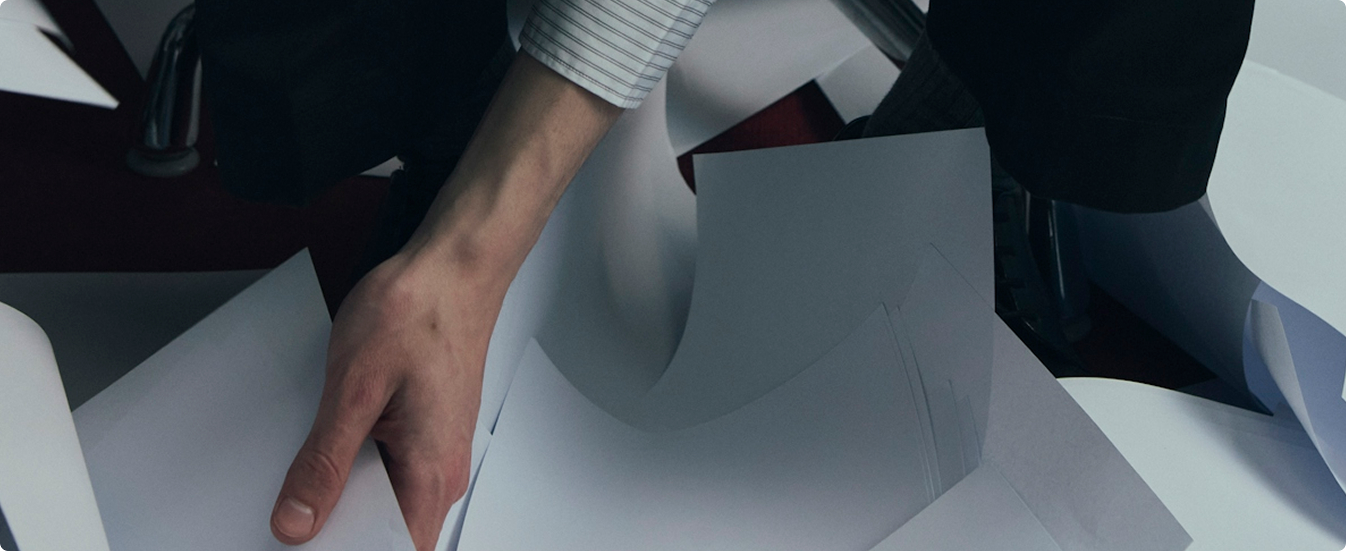 Main d'une personne triant plusieurs feuilles de papier blanches dispersées.