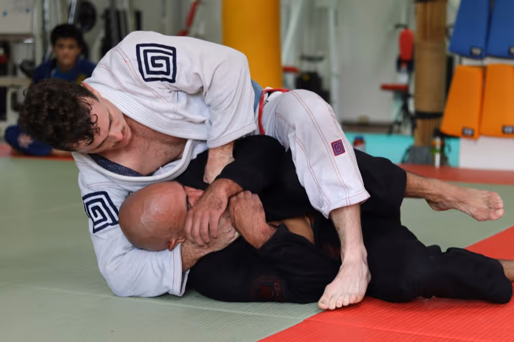 Two men practicing Brazilian jiu-jitsu grappling on a mat in a gym.