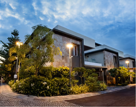 Modern residential buildings with stone facades and lush greenery under a cloudy evening sky.