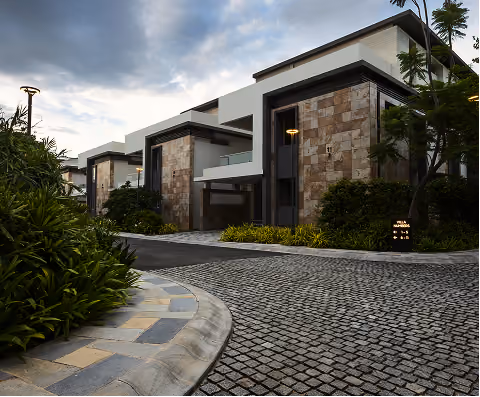 Modern houses with stone walls along a cobblestone street under a cloudy sky.