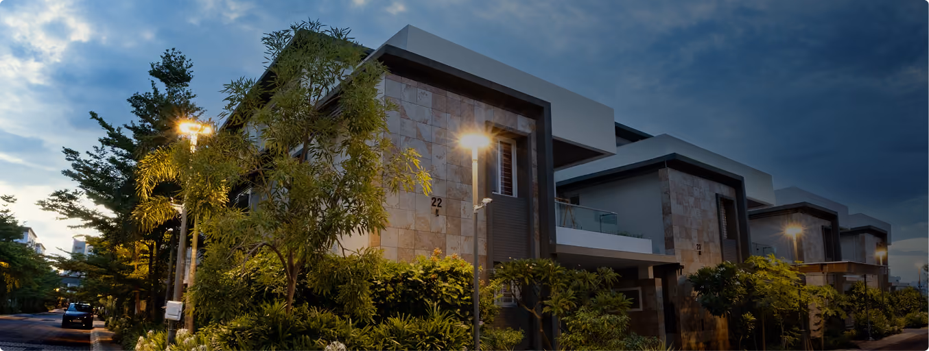 Modern two-story homes with stone facades set along a street lit by lamp posts at dusk.