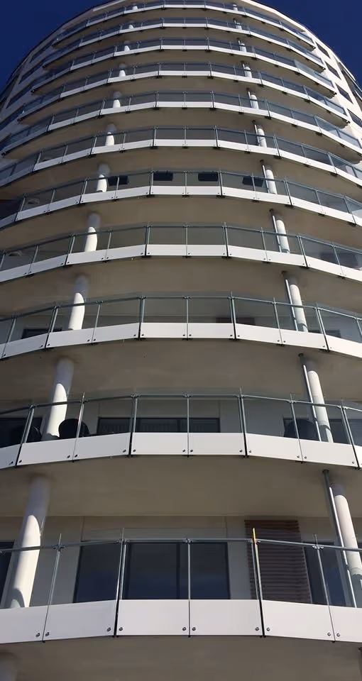 Moderne højhus med gentagne buede altaner og glasrækværk mod klar blå himmel.