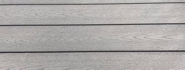 Nærbillede af fire parallelt arrangerede, grå træplanker med tydeligt kornmønster.