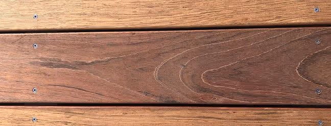 Nærbillede af mørkt, poleret træ med synlige åretegninger og skruer monteret i en vandret række.