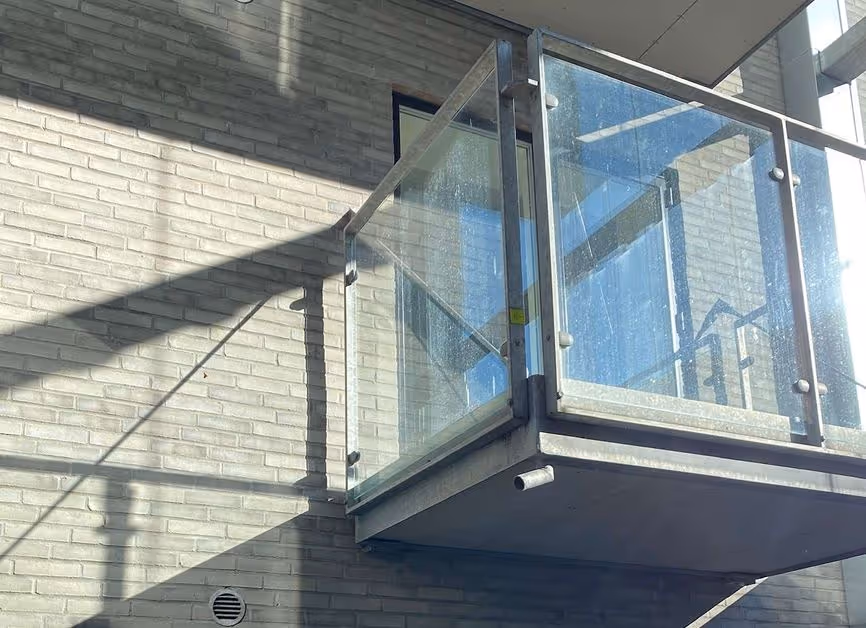 Glasdør med metalramme i moderne bygning, sollys kaster skygger på murstensvæggen.