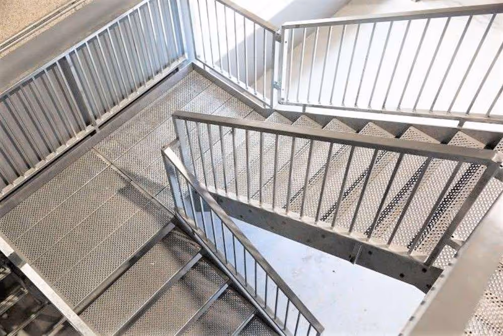 Metaltrappeopgang med reposer og gelænder set ovenfra i lyst miljø.