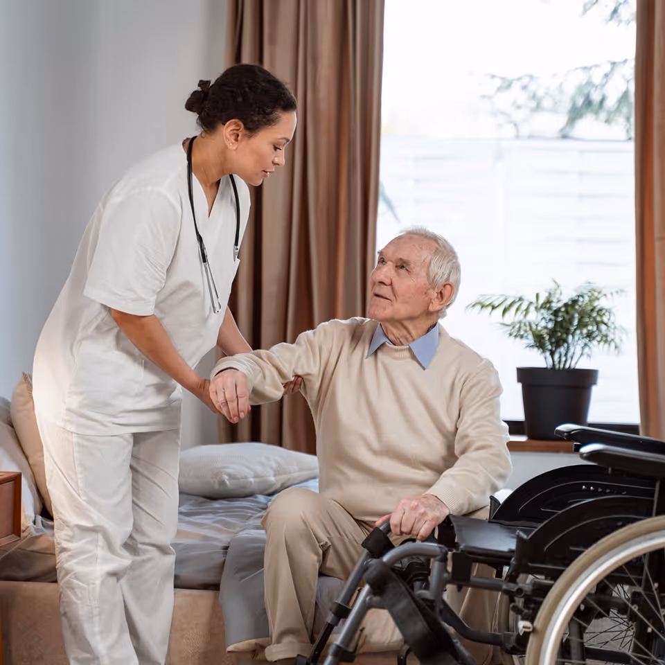 Elderly man with glasses playing a board game with red and white pieces at a wooden table indoors.