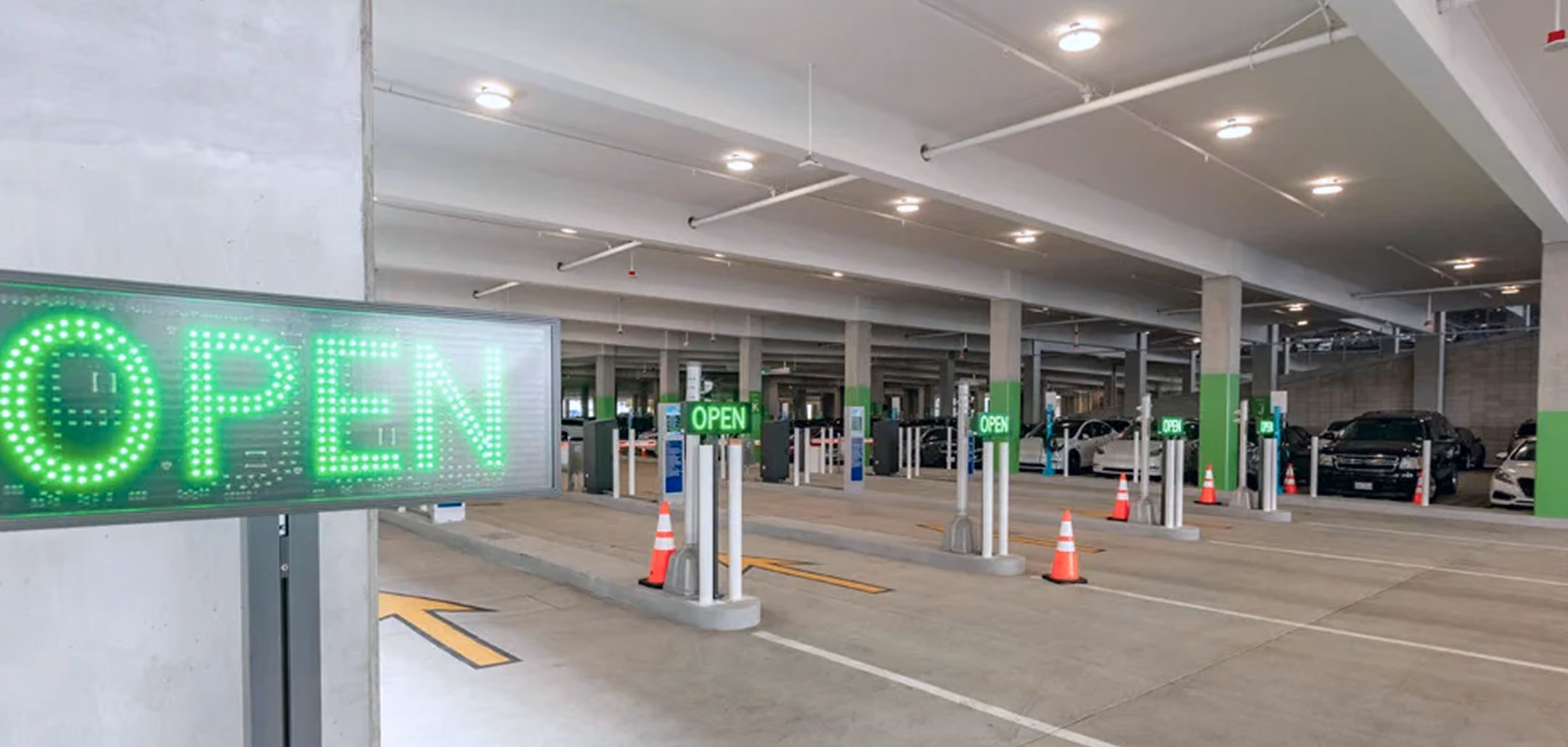Indoor parking garage entrance with multiple lanes marked by green illuminated OPEN signs and orange traffic cones.