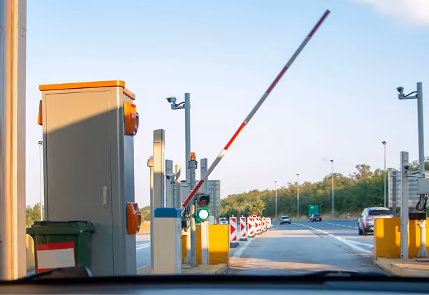 Toll booth barrier arm raised with a green traffic light on a sunny highway entrance.