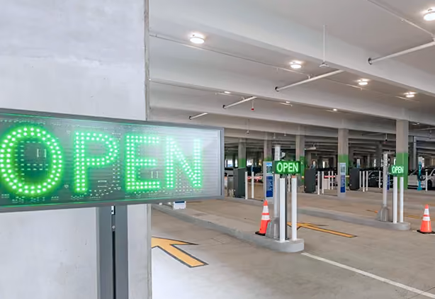 Green illuminated OPEN signs at the entrance lanes of a multi-level parking garage.