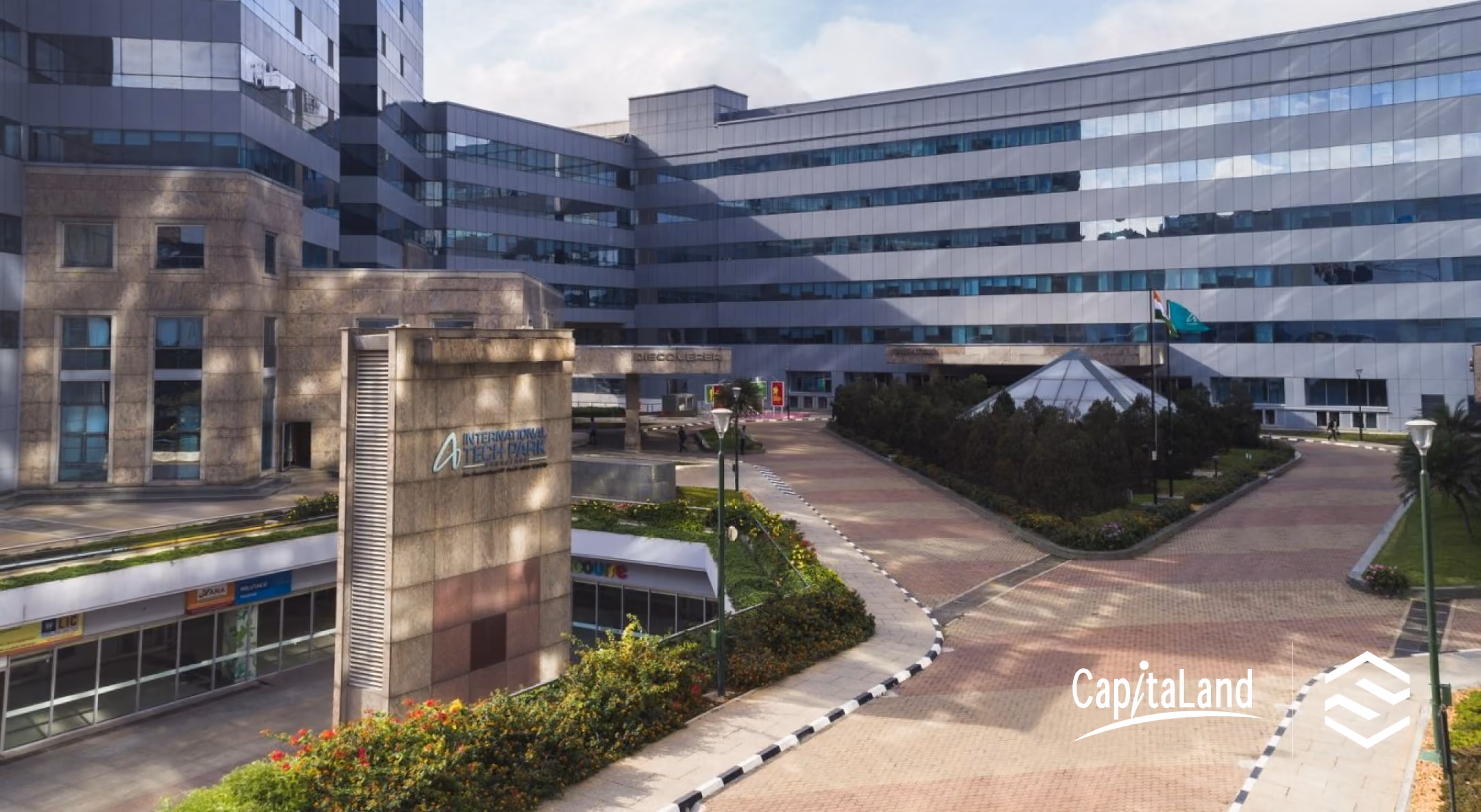 Modern office complex with glass and stone buildings, landscaped gardens, and pathways.