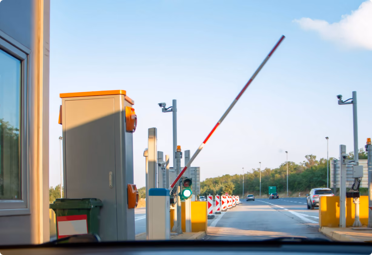 View from inside a car approaching a toll gate with a raised barrier and a green traffic light on a clear day.
