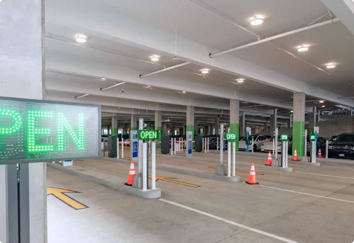 Indoor parking garage with multiple lanes marked by green LED ‘OPEN’ signs and orange traffic cones.