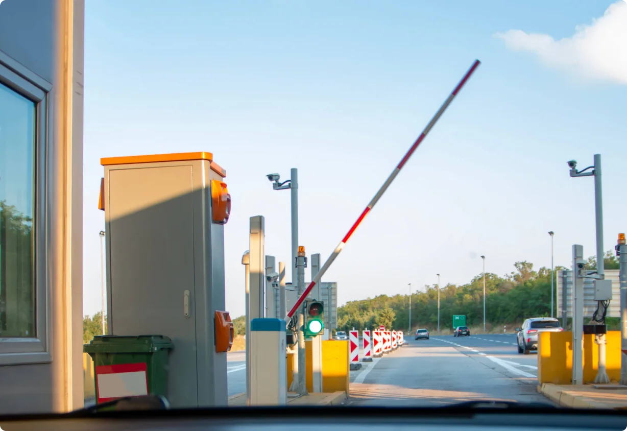 View from car approaching toll gate with raised barrier and green traffic light on a clear day.