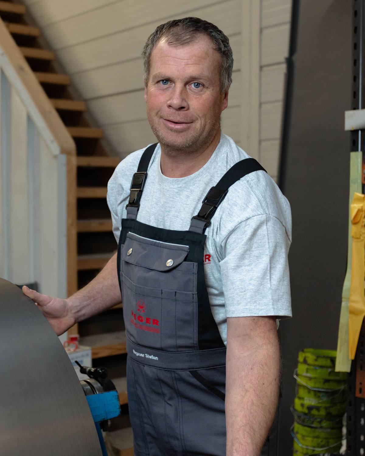 Handwerker in grau-schwarzer Arbeitskleidung in Werkstatt neben Metallrolle.