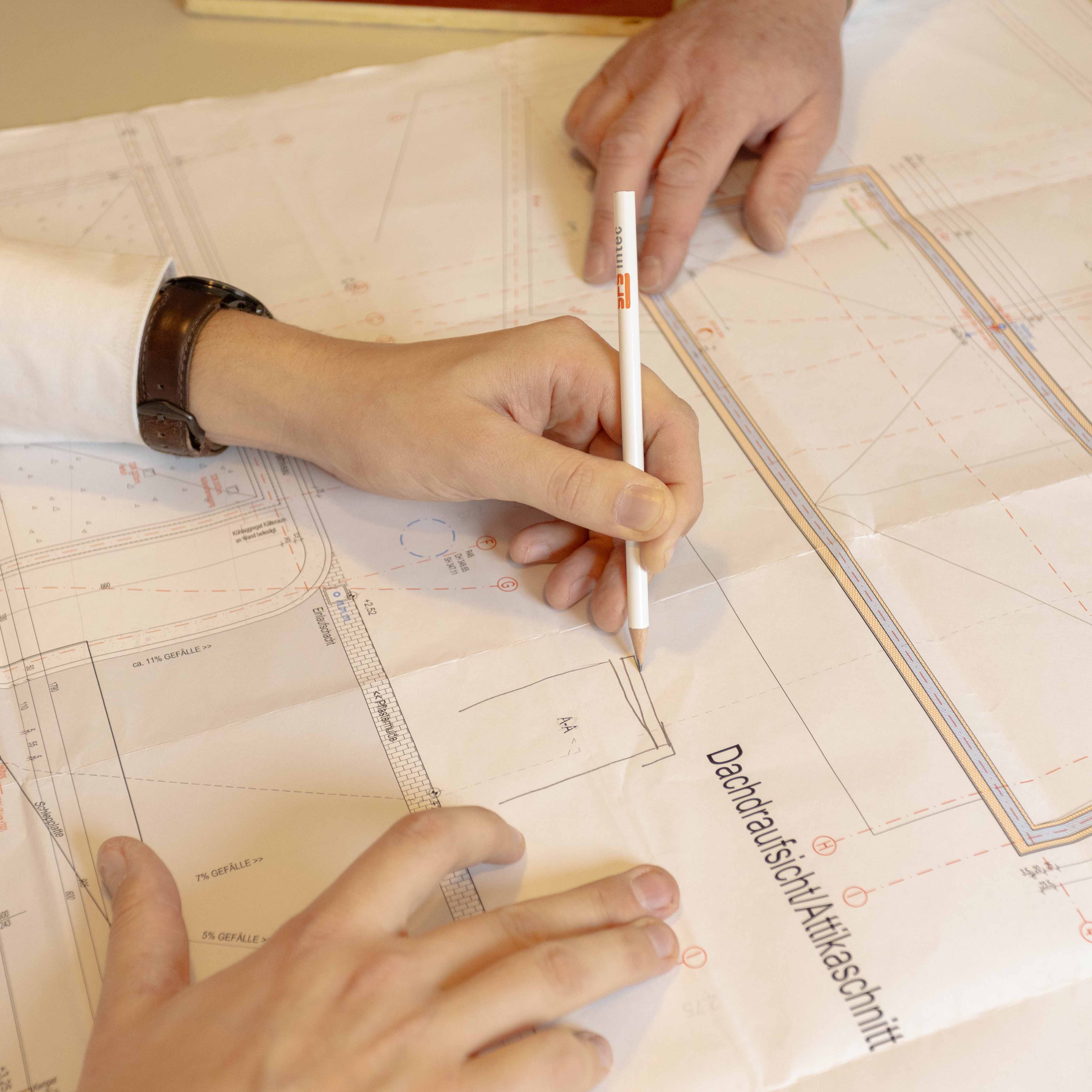 Hände zeichnen und zeigen auf einen Architekturplan mit dem Titel Dachtraufsicht/Atkiaschnitt.