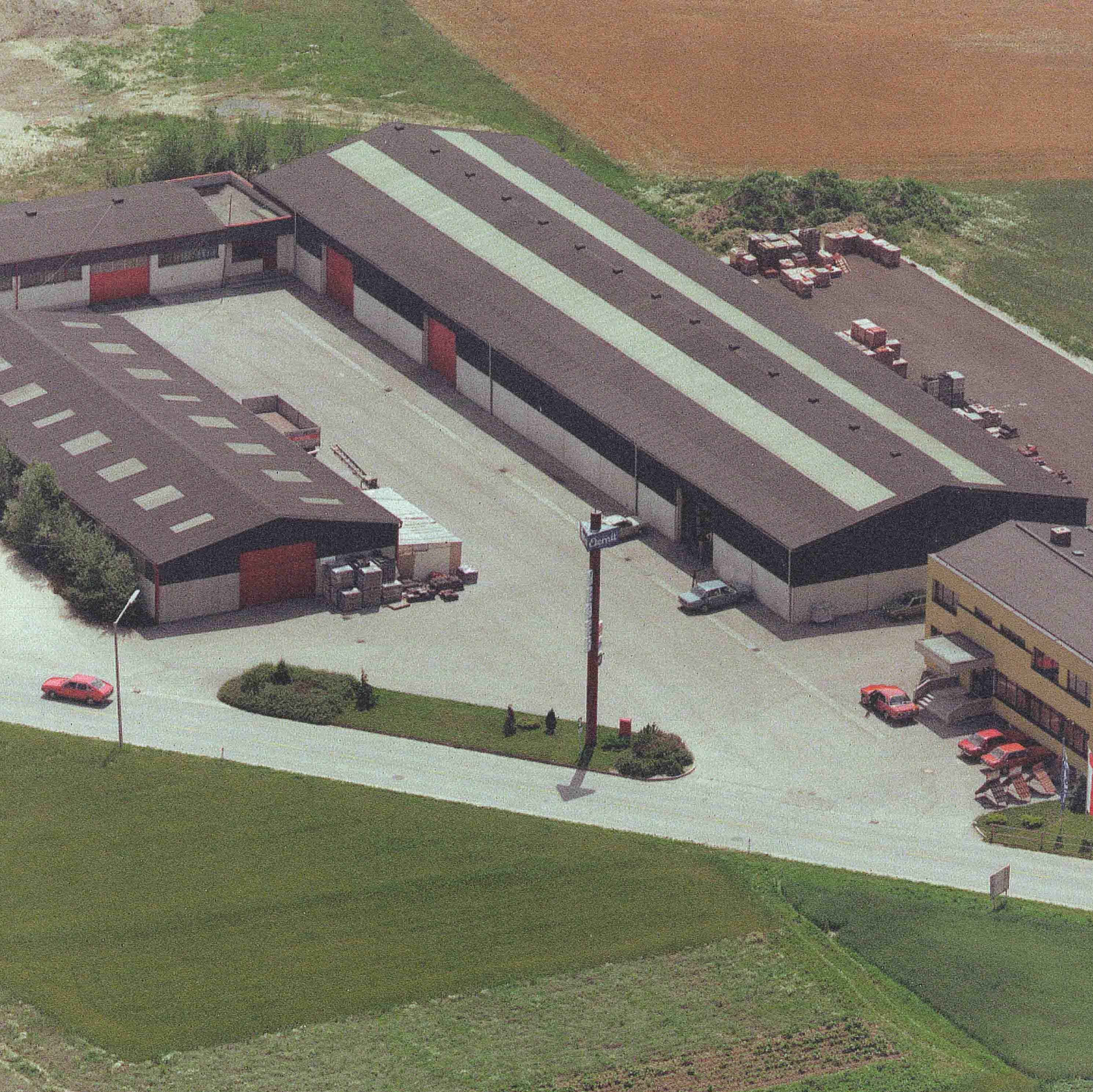 Luftaufnahme eines Industriegebiets mit mehreren Lagerhallen, Parkplätzen und landwirtschaftlichen Feldern.